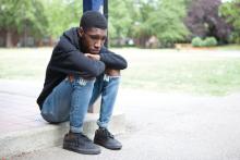 A sad teen sits on a curb